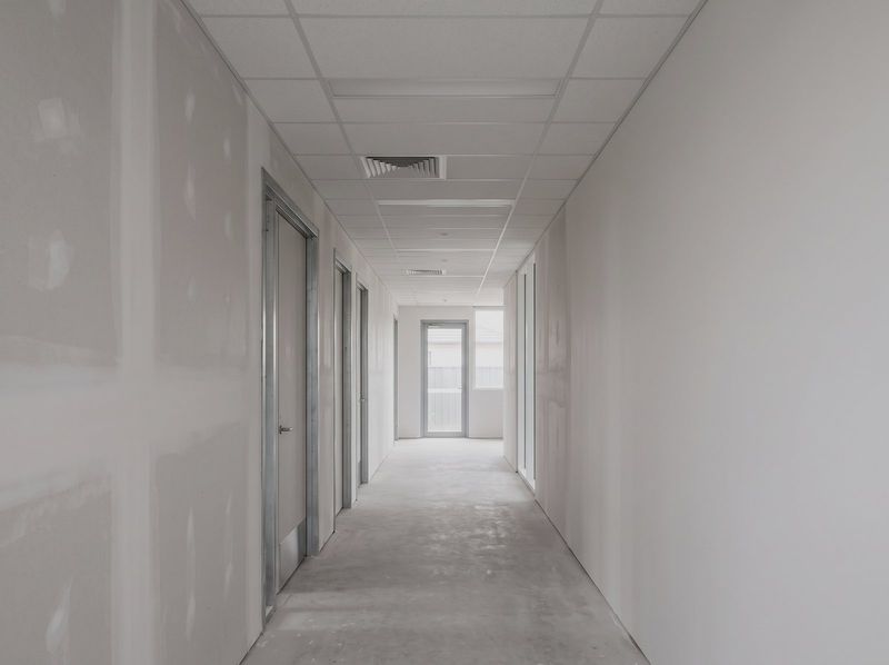 Commercial corridor with plasterboard walls set and sanded beneath a flush suspended ceiling