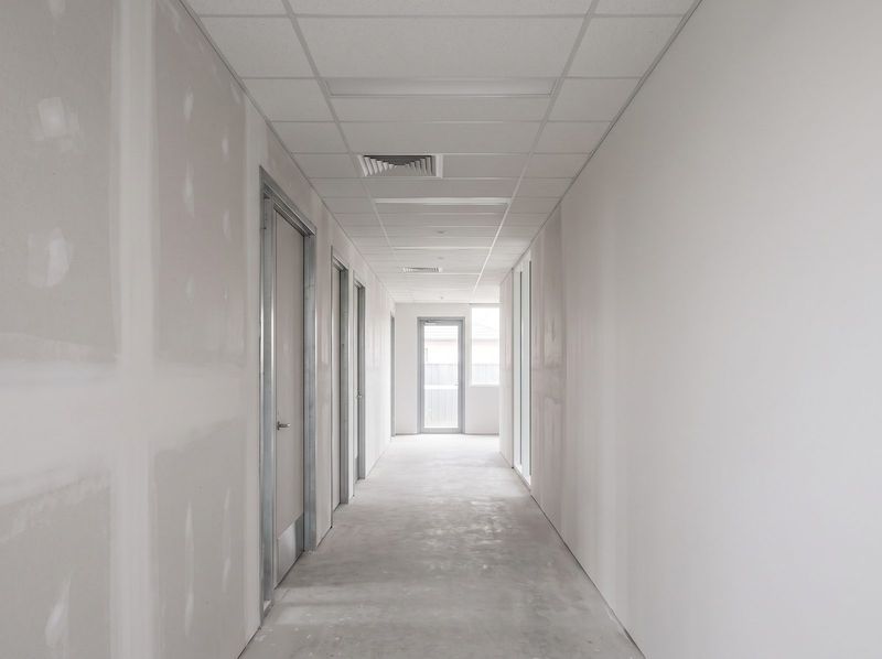 Commercial corridor with an exposed grid suspended ceiling, lay-in tiles installed and a supply air diffuser set into the grid, steel door frames down one side