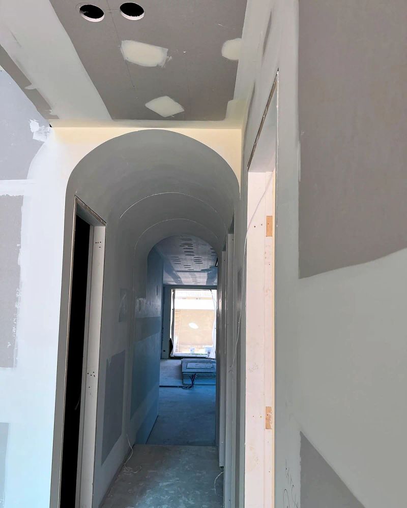 Barrel vaulted hallway with the arch sheeted and the joints set, patches and downlight cut-outs still showing before sanding