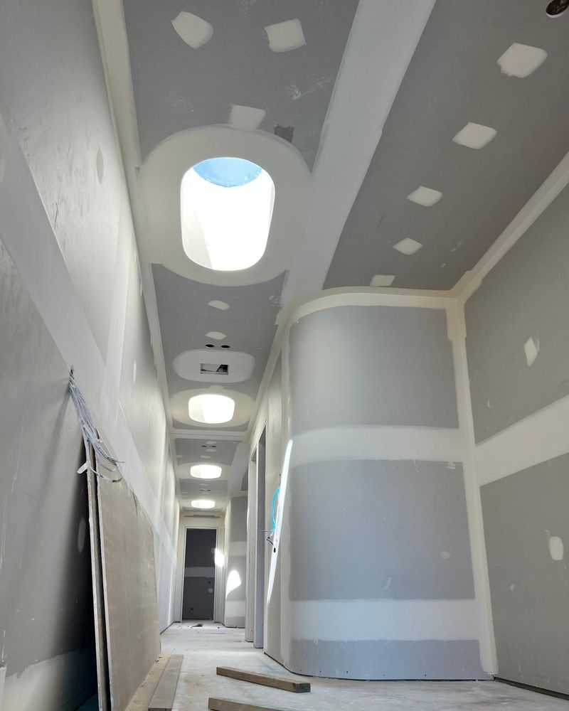 Oval skylight formed through a vaulted hallway ceiling, the curved reveal set and awaiting sanding