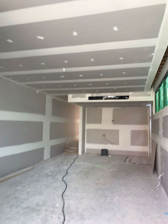 Suspended plasterboard ceiling sheeted and set with a bulkhead drop and a recessed linear light fitting, surrounding walls set and patched ready for the painter