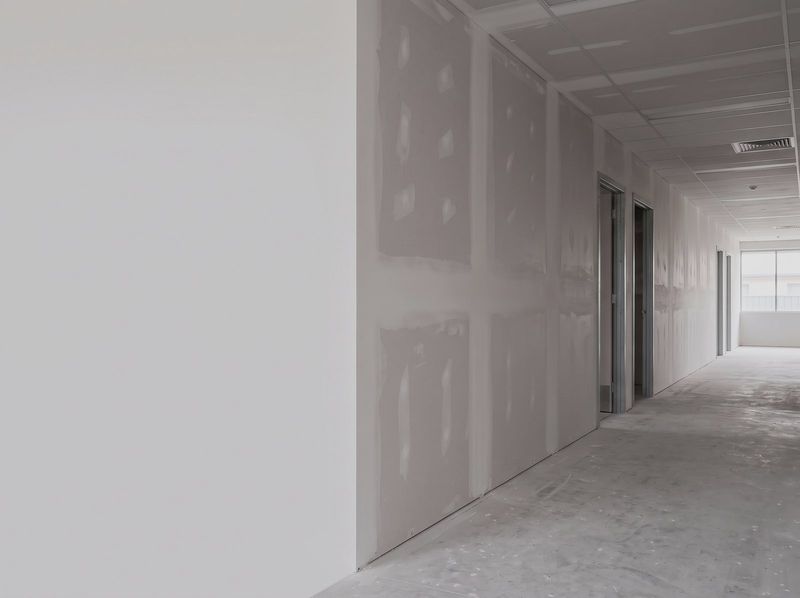 Commercial corridor with plasterboard walls sheeted and set, steel door frames and daylight from a window at the far end