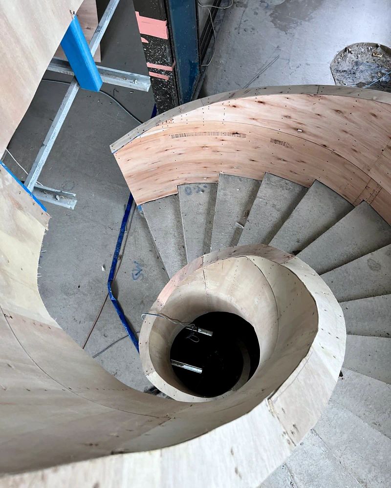 Helical staircase seen from above, the curved plywood formwork built and braced around the open stair void before any plaster goes on