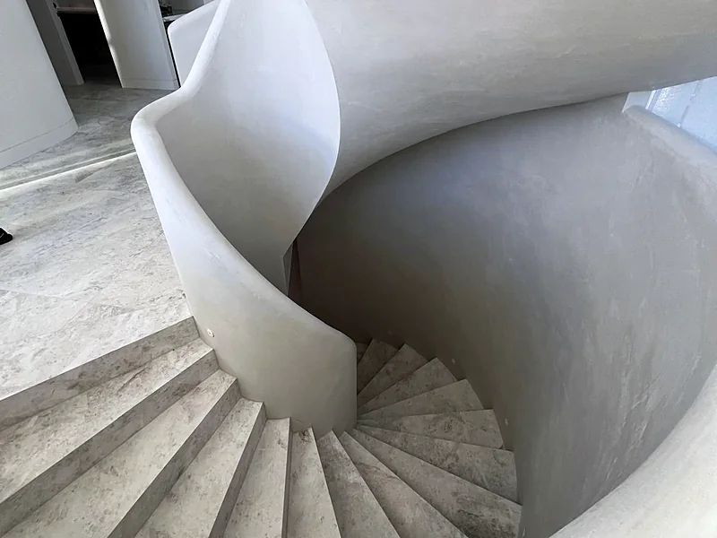 Helical staircase finished in solid plaster, the curved balustrade sweeping down to stone treads