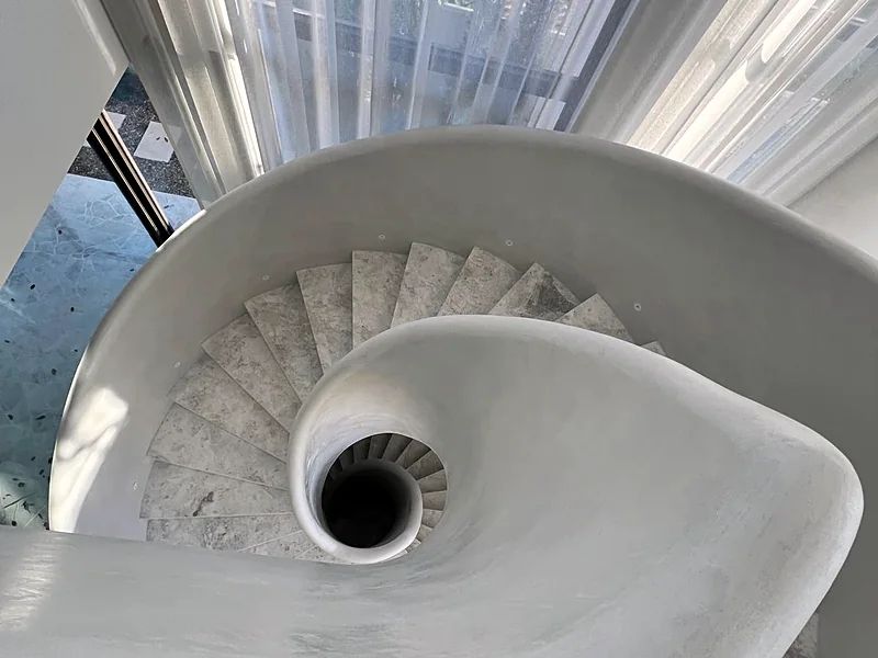 The same staircase from above, the balustrade finished in solid plaster and sweeping unbroken around the void to the concrete treads